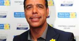 Chris Kamara smiling at a charity event, wearing a dark blazer and a yellow flower pin, promoting cancer awareness.