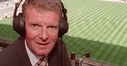 Football commentator wearing headphones in a broadcast booth, ready to provide live analysis during a match.