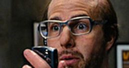 Les Grossman from Tropic Thunder, holding a phone, showcasing his iconic bald look and glasses in a comedic scene.