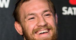 Conor McGregor smiles confidently during a press conference, showcasing his stylish suit and iconic beard.