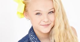 Smiling girl with blonde, wavy hair and a bright yellow bow, wearing a denim vest with rhinestones, embodies JOJO style.