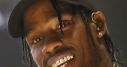 Travis Scott grinning on stage, showcasing his signature style with chains, a cap, and sparkling grills in a vibrant performance.