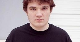 Young man with curly hair wearing a black "Rage Quit" t-shirt, standing confidently against a neutral background.