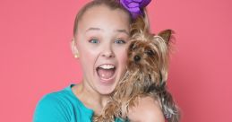 Joyful girl with a large purple bow, wearing a Jojo-themed shirt, holds a small dog against a bright pink background.