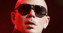 Pitbull performs on stage wearing sunglasses and a black suit, exuding confidence and energy under vibrant lighting.