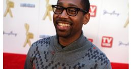 PJ Morton smiling at a red carpet event, wearing a stylish sweater, showcasing his engaging personality and fashion sense.