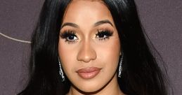 Cardi B poses elegantly with long black hair and glamorous makeup at a high-profile event, showcasing a stunning black dress.