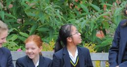 Girls in blazers and skirts sitting on a bench, enjoying a conversation in a lush garden at a Girls’ Grammar School.