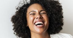 Joyful woman with curly hair laughing heartily, radiating happiness in a casual setting, showcasing the power of laughter.