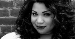 Confident woman with curly hair poses against a brick wall, showcasing bold style and self-expression in black and white.