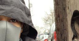 Person wearing a gray mask and coat sits beside a dog on a city street, with cars parked in the background.