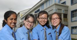 Four girls in blue school uniforms demonstrating friendship and teamwork outside a secondary school on a sunny day.