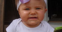 Nine-month-old baby girl in a white onesie with a "9 Months" badge, wearing a purple bow, smiling happily.