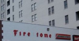 Signage of "Fire Tone" on a building with parked cars and yellow safety poles in an urban setting.