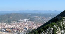 Panoramic view of Gibraltar's cliffs, showcasing the lush greenery and urban landscape under a clear blue sky.