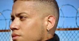 Confident individual in leather attire with a distinct earring, showcasing a bold expression against a barbed wire backdrop.