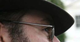 Man wearing a gray hat and glasses, smoking a pipe, showcasing a classic Welsh Chief V1 style with distinctive sideburns.