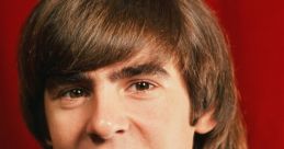 Young Davy Jones with a polka dot shirt, smiling against a red background, showcasing his iconic 1960s hairstyle.