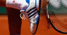 Tennis player in blue and white shoes kicks up clay on the court while preparing to swing their racket.