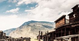 Rustic wooden wagon in an abandoned Wild West town, surrounded by mountainous scenery and dusty trails under a cloudy sky.