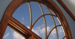 Elegant wooden arch window with detailed trim, showcasing clear blue sky and clouds, enhancing interior aesthetics.