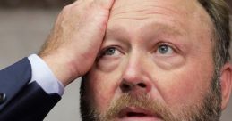 Alex Jones looking distressed, hand on forehead, during a tense moment in a public appearance or court hearing.