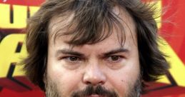 Jack Black with tousled hair and beard, wearing a graphic T-shirt at a vibrant event backdrop, exuding charisma and humor.