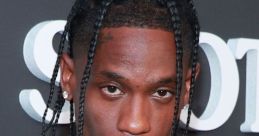 Travis Scott at a red carpet event, showcasing his unique fashion style with braided hair and a serious expression.