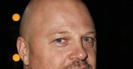 Michael Chiklis with a shaved head, wearing a leather jacket, striking a serious pose against a dark background.