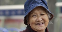 Smiling elderly Chinese woman wearing a traditional coat and denim bucket hat, conveying warmth and joy in her expression.