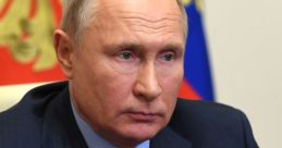 Vladimir Putin seated at a table, looking serious with a focused expression, in front of the Russian flag backdrop.