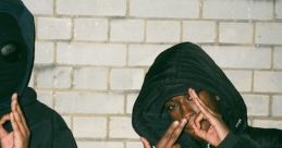 Two individuals in hooded jackets pose against a brick wall, showcasing a street style vibe influenced by UK drill culture.