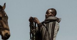 Man in traditional attire prepares horse reins in a scenic landscape, showcasing bond between humans and animals.