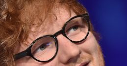 Ed Sheeran with glasses, smiling at an event, showcasing his signature style and charismatic personality.