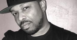 DJ Scratch poses confidently in a black t-shirt and cap, showcasing his passion for music and turntablism.