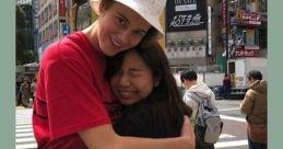 Two friends share a warm hug in a busy city, expressing humor about watching Ruel videos instead of studying.