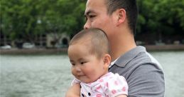 Father holding smiling baby by the lakeside, showcasing a joyful moment and bonding experience in a serene environment.