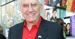 Ed McMahon smiling at a red carpet event, wearing a black suit and red shirt, exuding charisma and charm.