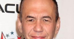 Gilbert Gottfried smiling at an event, showcasing his signature humor and charisma against a branded backdrop.