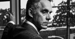 Jordan Peterson poses thoughtfully by a rain-streaked window, embodying a contemplative mood in a stylish suit.