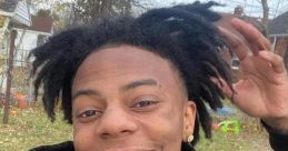 Young man with stylish dreadlocks smiles in a casual "IShowSpeed" hoodie, showing vibrant personality outdoors.