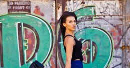 Fashionable model Codie Phillips struts in sheer blue pants and heels against vibrant graffiti backdrop, showcasing trendy urban style.