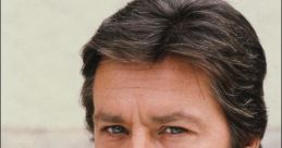 Close-up of a handsome man with dark hair and blue eyes, thoughtful expression, wearing a casual outfit and wristwatch.