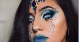 Glamorous water-themed makeup with blue tones, jeweled accents, and dramatic tear designs for a stunning creative look.