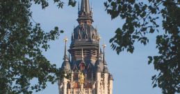 Historic bell tower with intricate architecture framed by lush greenery against a clear blue sky.