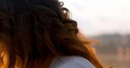 Woman with flowing hair seated by a tranquil waterfront, reflecting on themes of loyalty and connection at sunset.