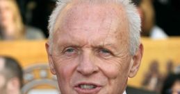 Anthony Hopkins smiles at a red carpet event, dressed in a classic black suit and tie, showcasing his iconic style.