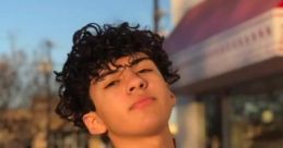 Portrait of a young Hispanic male with curly hair, wearing a white shirt, standing outdoors in warm sunlight.