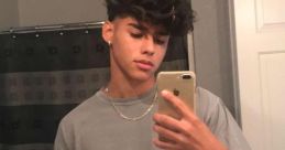 Young Hispanic male taking a selfie in a bathroom mirror, wearing a grey shirt and a chain, captioned "Wednesday.