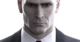 Agent 47, portrayed by David Bateson, exudes a cool, intimidating presence in a formal suit with a red tie.